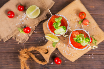 Two glasses of tomato juice decorated with fresh tomatoes, cucumber and leaves on a wooden background