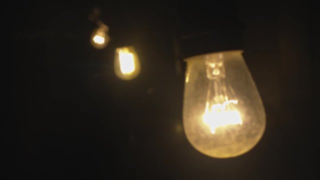 Focus pull on line of light bulbs glowing outside in the garden at night.