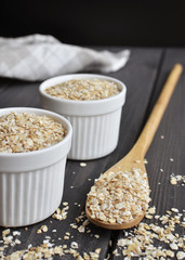Rolled oats in bowls and spoon on dark wooden table background