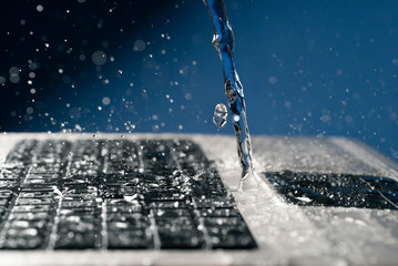 A stream of water pours on the laptop keyboard. - obrazy, fototapety, plakaty