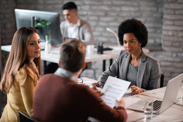 Black female bank manager talking to a couple about their loan application on a meeting.