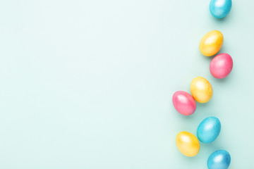 Border made of colorful Easter eggs on turquoise background. Top view, copy spase, minimal styled.