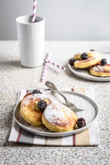 Homemade curd fritters with berries and a cup of milk on a gray background. Healthy and diet breakfast