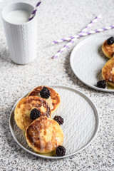 Homemade curd fritters with berries and a cup of milk on a gray background. Healthy and diet breakfast