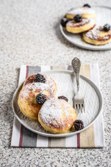 Homemade curd fritters with berries and a cup of milk on a gray background. Healthy and diet breakfast