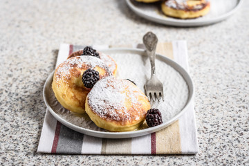 Homemade curd fritters with berries and a cup of milk on a gray background. Healthy and diet breakfast