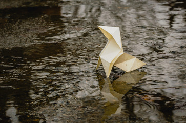 Origami paper figure on the background of a gloomy city street and puddles