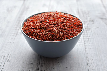 Fototapeta na wymiar Bowl with uncooked red rice on wooden background