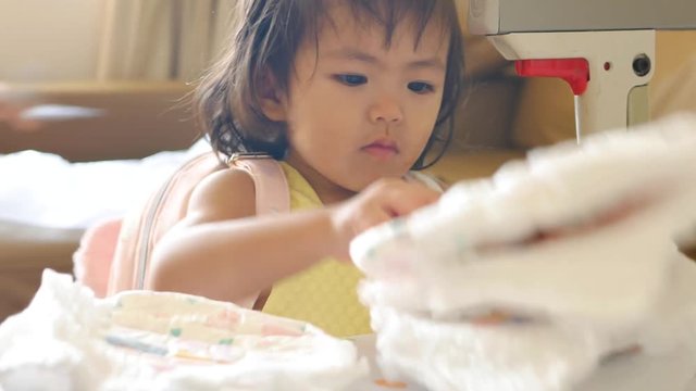 Little Asian baby girl, 22 months old, playing / learning to arrange / stack up her diapers in pile