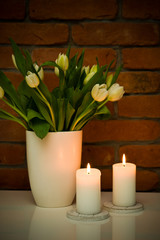 White tulips bouquet in a vase against red brick wall.