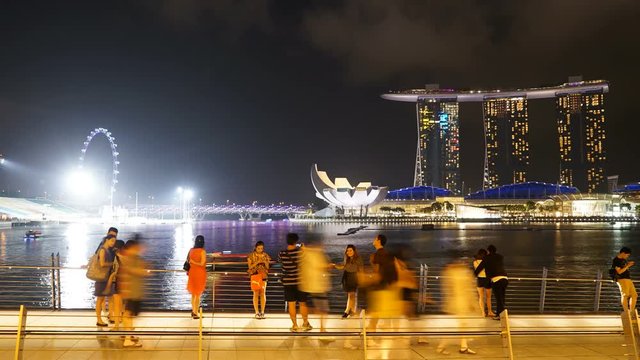 Medium wide angle dolly out timelapse video of people at merlion park, Singapore with the marina bay sands casino and Singapore flyer in the background during night time