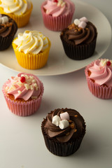Colorful cupcakes on a white background. Pink, yellow and chocolate cupcakes. Party food. Sweet dessert or breakfast. Party, birthday food. Bright food photo.