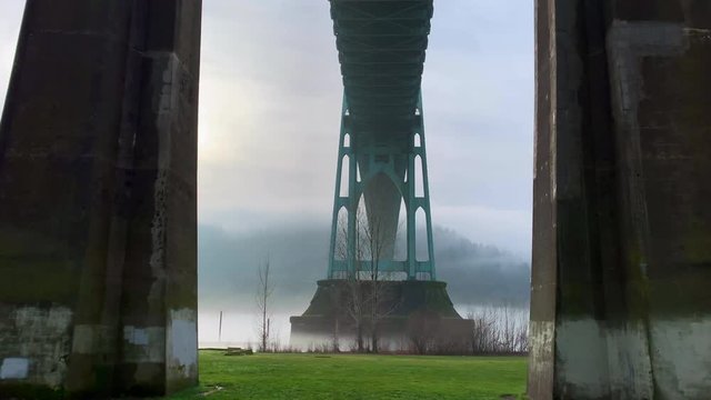 Amazing scenery of first person walking under a bridge between the pillars, beautiful landscape, mountains, cloudy sky. St Johns bridge, Portland, Oregon.