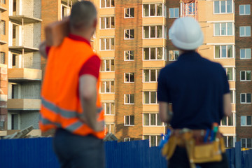 Two engineer builders with blueprint plan at construction site