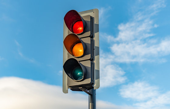 An English traffic light sits isolated against a bright blue sky with the red, orange and green lights