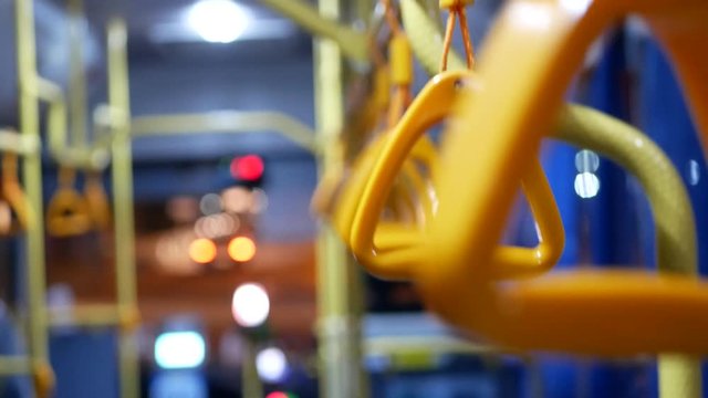 Selective focus of shaking pivoted grab handles on a moving shuttle bus, traveling on a street at night - public transportation