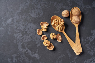 Walnuts  in two wooden spoons on black table, with copy space. Top view.