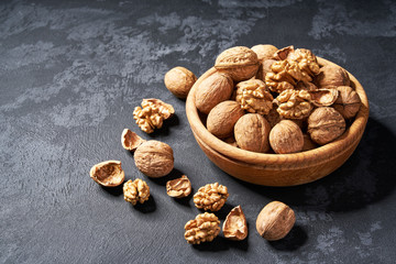 Organic walnut in wooden bowl on black background, close-up.