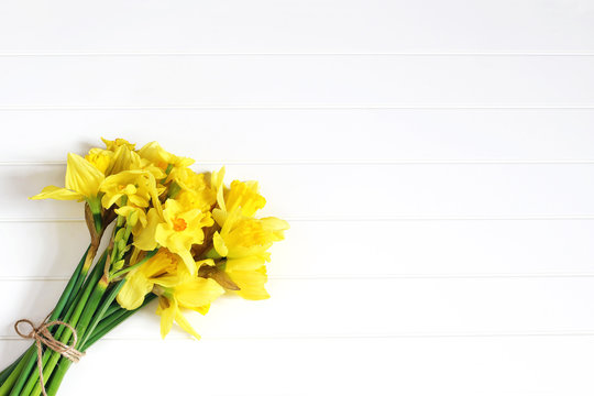 Easter greeting card, invitation. Bouquet of yellow daffodils, narcissus flowers lying on white wooden table. Spring concept. Feminine styled stock photo, floral composition. Flat lay, top view.