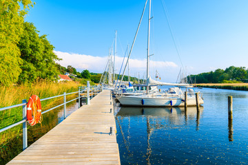 Wooden pier with sailing boats anchoring on beautiful lake in Moritzdorf village on coast of Rugen island, Baltic Sea, Germany