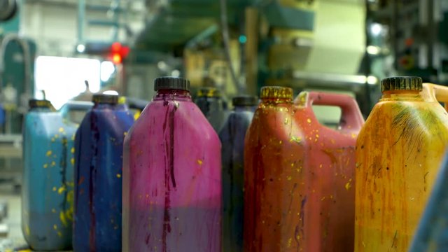 Closeup of a group of paint-splatterd containers. A male hand appears and places a violet container among the other containers.