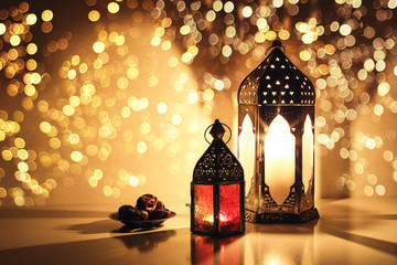 Ornamental Arabic lanterns with burning candles. Glittering golden bokeh lights. Plate with date fruit on the table. Greeting card for Muslim holiday Ramadan Kareem. Iftar dinner background.