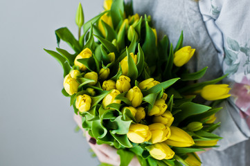 Girl florist holding a bunch of yellow tulips. Floristic. Gray background