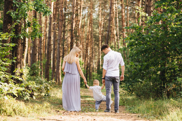 Happy young family spends time together in nature. Parents go and hold the child's hands