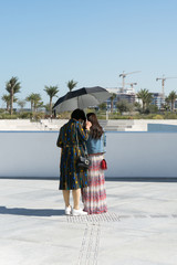 two Japanese tourists standing under an umbrella in the sunshine