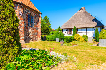 Fototapeta na wymiar Traditional house with straw roof and old gothic church built from red bricks in Middelhagen village, Ruegen island, Baltic Sea, Germany