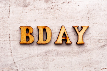 Inscription BD BDAY birthday abbreviation in wooden letters on a light background