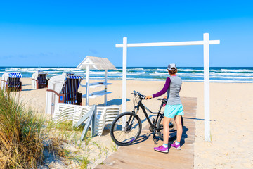 Young woman with bicycle standing on path to beautiful sandy beach in Baabe on Rugen island, Baltic...