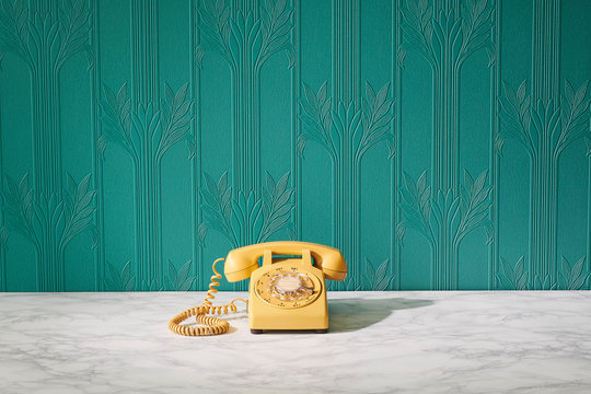 Vintage Retro Yellow Rotary Telephone on Marble Table with Teal Blue Green Wall Floral Pattern Paper