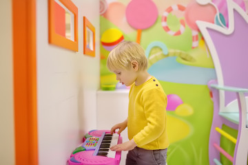 Little boy having fun in amusement in play center. Baby playing on a toy piano at kids children's playroom.