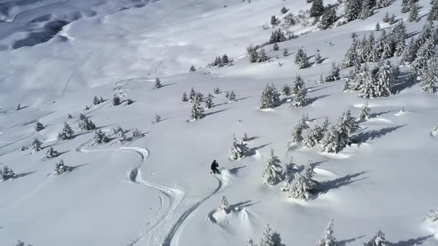 Aerial view tracking a snowboarder from above, off piste in fresh snow in the French Alps in winter.
