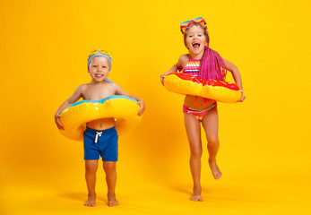 happy children girl and boy in swimsuit with swimming ring donut on colored yellow background.