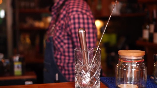 Close up slow motion view on bartending instruments next to glass jars with spices on wooden bar counter