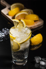 Gin tonic with lemon slices and ice cube, with lemon and ice for decorate on back, on the black background