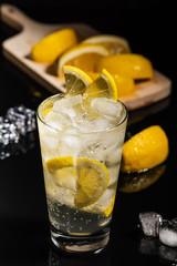 Gin tonic with lemon slices and ice cube, with lemon and ice for decorate on back, on the black background