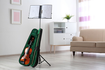 Violin in case and note stand with music sheets in room