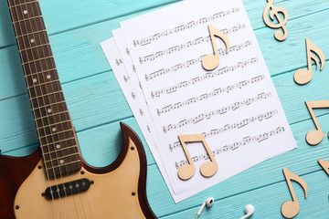 Fototapeta na wymiar Guitar neck and sheets with music notes on color wooden background, flat lay