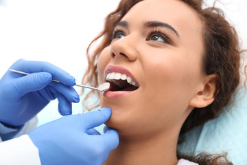 Dentist examining African-American woman's teeth with mirror in hospital
