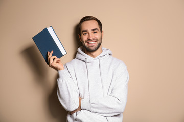 Young happy man with book on color background