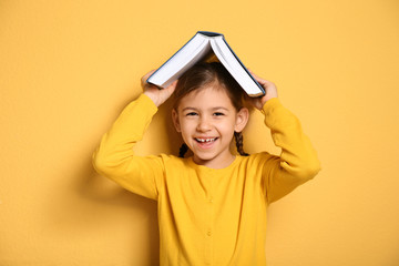 Cute little girl with book on color background