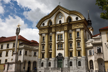Fototapeta na wymiar Spot of sun on the Ursuline Church of the Holy Trinity with marble statues of the Holy Trinity column in Ljubljana Slovenia with dark clouds