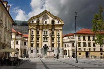 Fototapeta na wymiar Ursuline Church of the Holy Trinity with marble statues of the Holy Trinity column at Congress Square in Ljubljana Slovenia with dark clouds