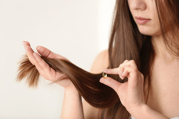 Woman holding vitamin capsule for hair health on light background, closeup