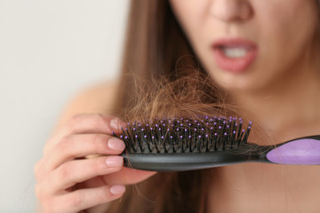Woman untangling her hair from brush on light background, closeup