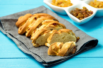 Piece of Sweet Braided Bread with raisins on kitchen towel on blue wooden background.