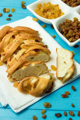 Piece of Sweet Braided Bread with raisins on kitchen towel on blue wooden background.